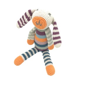 Peut inclure: Un jouet en crochet en forme de lapin ray&eacute; avec un visage blanc et un nez orange. Le lapin est assis les pattes tendues.