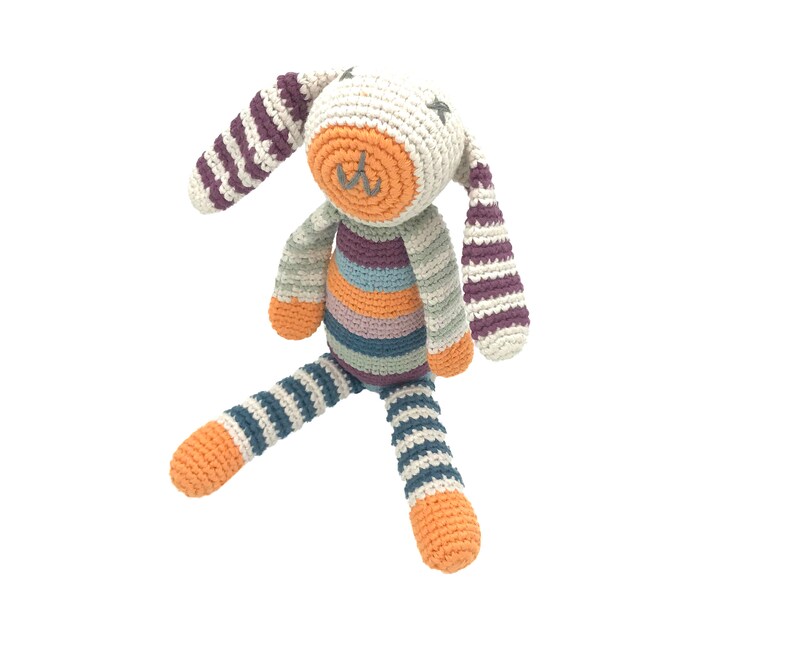 Peut inclure: Un jouet en crochet en forme de lapin ray&eacute; avec un visage blanc et un nez orange. Le lapin est assis les pattes tendues.