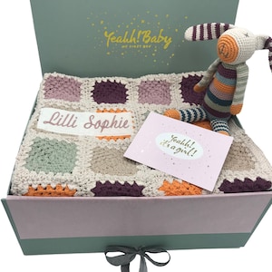 Könnte beinhalten: Eine grüne Geschenkbox mit einer rosa-weißen Häkeldecke, einem gestreiften Häkelhasen und einer rosa Karte mit der Aufschrift "Yeahh! Es ist ein Mädchen!" Die Decke hat ein personalisiertes Namensschild mit der Aufschrift "Lilli Sophie".