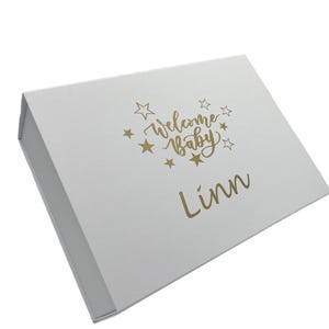 Peut inclure: Bo&icirc;te cadeau blanche avec inscription dor&eacute;e "Welcome Baby Linn" entour&eacute;e d'&eacute;toiles.