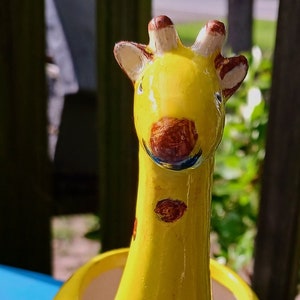 May include: A whimsical, yellow ceramic giraffe planter with brown spots. The giraffe has a long neck, a round body, and small feet. The planter is designed to hold small plants or flowers, adding a touch of fun to any space.