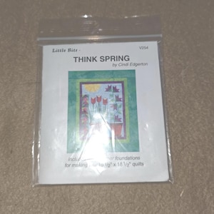 May include: A clear plastic package containing a quilt pattern titled "THINK SPRING" by Cindi Edgerton. The pattern features a colorful floral design with the text "Little Bitz" at the top. The quilt size is 48 1/2" x 18 1/2".