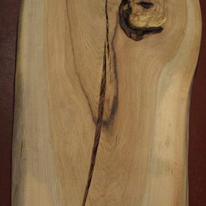 May include: A large piece of light brown wood with a natural edge and a knot in the center. The wood has a smooth surface and a light grain pattern.