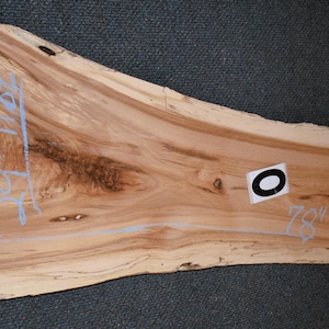 May include: A live edge wood slab with natural grain patterns. The slab is approximately 78 inches long and 20 inches wide. The wood has a light brown color with darker brown streaks and knots.