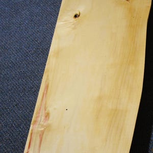May include: A large, light wood plank with a natural, unfinished surface. The wood has a reddish-brown hue in some areas, creating a unique pattern.