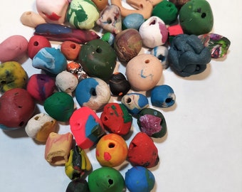 May include: A collection of colorful clay beads in various shapes and sizes, including round, oval, and irregular shapes. The beads are made of polymer clay and have a variety of colors, including red, green, blue, yellow, and white.