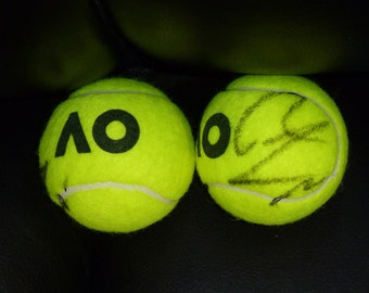 Könnte beinhalten: Zwei gelbe Tennisbälle, einer mit den Buchstaben "AO" bedruckt und der andere mit einer schwarzen Unterschrift.