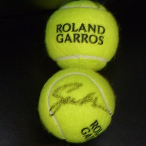 May include: Two yellow tennis balls, one with the words "Roland Garros" printed on it and the other with a signature.