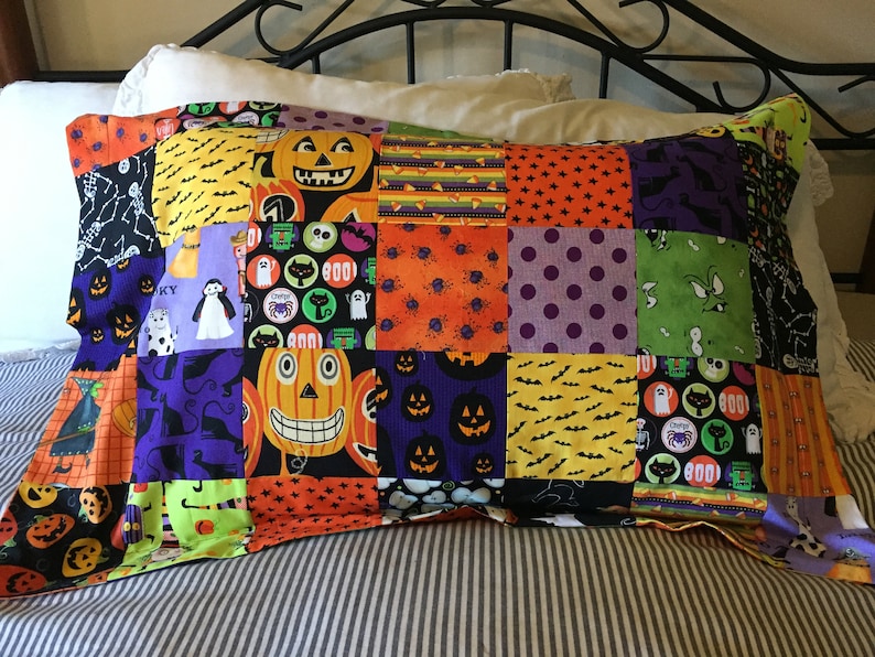 Puede incluir: Una funda de almohada de patchwork con tem&aacute;tica de Halloween. La funda de almohada est&aacute; hecha de cuadrados de tela con dise&ntilde;os de calabazas, murci&eacute;lagos, fantasmas y otros dise&ntilde;os espeluznantes en naranja, negro, morado y verde. La funda de almohada es rectangular.