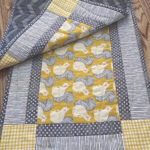 May include: A handmade quilt featuring a central panel of white llamas on a yellow background. The quilt is bordered with gray and white patterned fabrics, including stripes, polka dots, and a chevron design. The quilt is approximately 30 inches long and 20 inches wide.