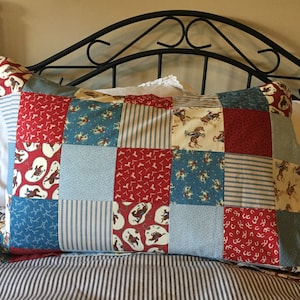 May include: A patchwork pillow with a western theme. The pillow is made of different fabrics with various patterns, including cowboys riding horses, horseshoes, and stripes. The pillow is blue, red, and beige.