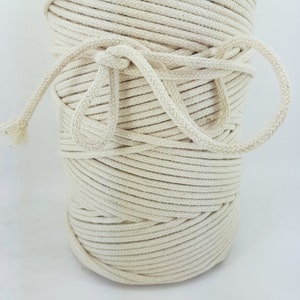 May include: A close-up of a spool of natural cotton cord. The cord is tightly wound and has a natural, off-white color.