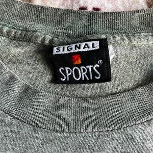 May include: A black and white label with the text "SIGNAL SPORTS" in white lettering. The label has a small red and orange logo in the upper left corner.