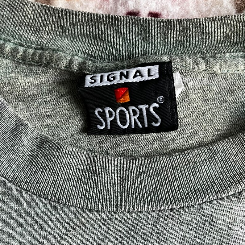 May include: A black and white label with the text "SIGNAL SPORTS" in white lettering. The label has a small red and orange logo in the upper left corner.
