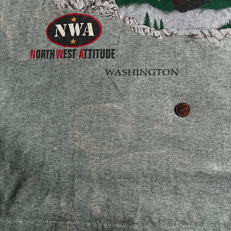 May include: Gray t-shirt with a red and white logo that says "NWA NORTHWEST ATTITUDE" and the text "WASHINGTON" below the logo.
