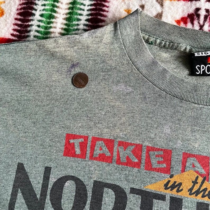May include: Gray t-shirt with red and black lettering that reads "Take Me North in the Wild".