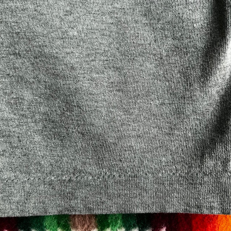 May include: Close-up of a gray knit fabric with a subtle texture. The fabric has a slight sheen and a smooth, soft feel.