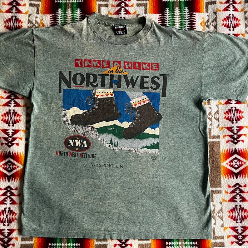 May include: A gray t-shirt with a graphic print of hiking boots and the text "Take a Hike in the Northwest" and "NWA North West Attitude Washington".