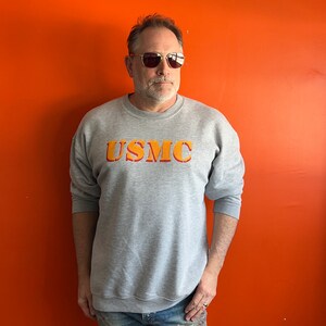 May include: A gray sweatshirt with the text "USMC" in orange and red letters.