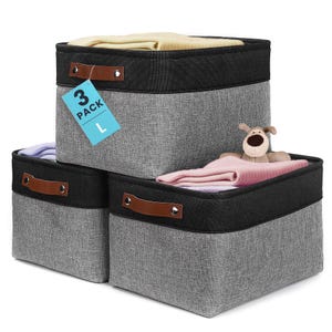 May include: A set of three square storage bins featuring a grey fabric body with a black fabric top border and brown faux leather handles secured with silver rivets. A blue tag attached to the top bin displays the text 3 PACK L in black.