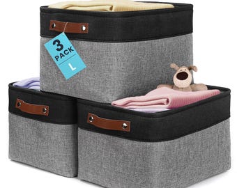 May include: A set of three square storage bins featuring a grey fabric body with a black fabric top border and brown faux leather handles secured with silver rivets. A blue tag attached to the top bin displays the text 3 PACK L in black.