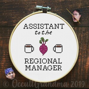 May include: A white embroidery hoop with black text that reads "Assistant to the Regional Manager" with a beet and two coffee cups in between the words. The text is in a pixelated font.