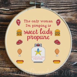 May include: A cross-stitch embroidery hoop with a yellow background and red text that reads "The only woman I'm pimping is sweet lady propane". The design includes a propane tank with a star and the text "Strickland Propane", as well as various food items like hamburgers, hot dogs, chicken legs, and steaks.