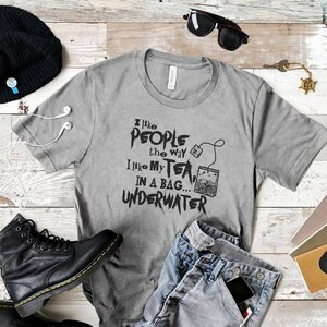 May include: A gray t-shirt with the text "I like people the way I like my tea... in a bag... underwater" printed on it. The text is in black and has a grunge-style font.