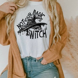 Puede incluir: Una camiseta blanca con un gráfico en blanco y negro de un sombrero de bruja y el texto "Not Your Basic Witch".