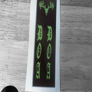 K&ouml;nnte beinhalten: Ein schwarzer und gr&uuml;ner Aufkleber mit einem Hirschsch&auml;del und dem Wort "DOA" in gotischer Schrift.