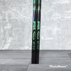 K&ouml;nnte beinhalten: Zwei schwarze Drumsticks mit gr&uuml;nen Akzenten. Die Drumsticks haben das Wort "DOOM" in gotischer Schrift.