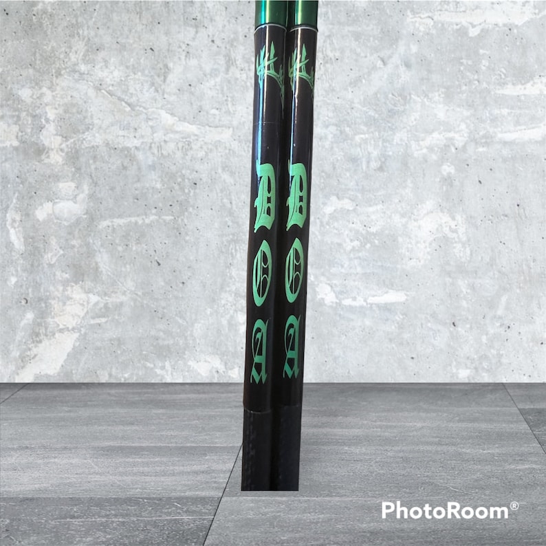 K&ouml;nnte beinhalten: Zwei schwarze Drumsticks mit gr&uuml;nen Akzenten. Die Drumsticks haben das Wort "DOOM" in gotischer Schrift.