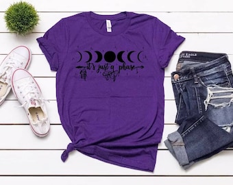 May include: Purple t-shirt with a black graphic of a crescent moon, full moon, and a quote that says "It's just a phase".