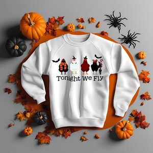 Puede incluir: Sudadera blanca con un gráfico de cinco pollos vestidos con disfraces de Halloween. Los pollos llevan sombreros, bufandas y otros accesorios. El texto "Tonight We Fly" está impreso debajo de los pollos.