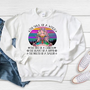 May include: White sweatshirt with a colorful graphic of a woman meditating in front of a sunset. The text "The Soul of a Witch" is above the graphic and the text "The Fire of a Lioness, The Heart of a Hippie, The Mouth of a Sailor" is below the graphic.