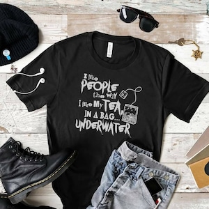 May include: Black t-shirt with white text that reads "I like people the way I like my tea... in a bag... underwater". The text is stylized to look like graffiti. There is a small image of a tea bag with a string attached to it.