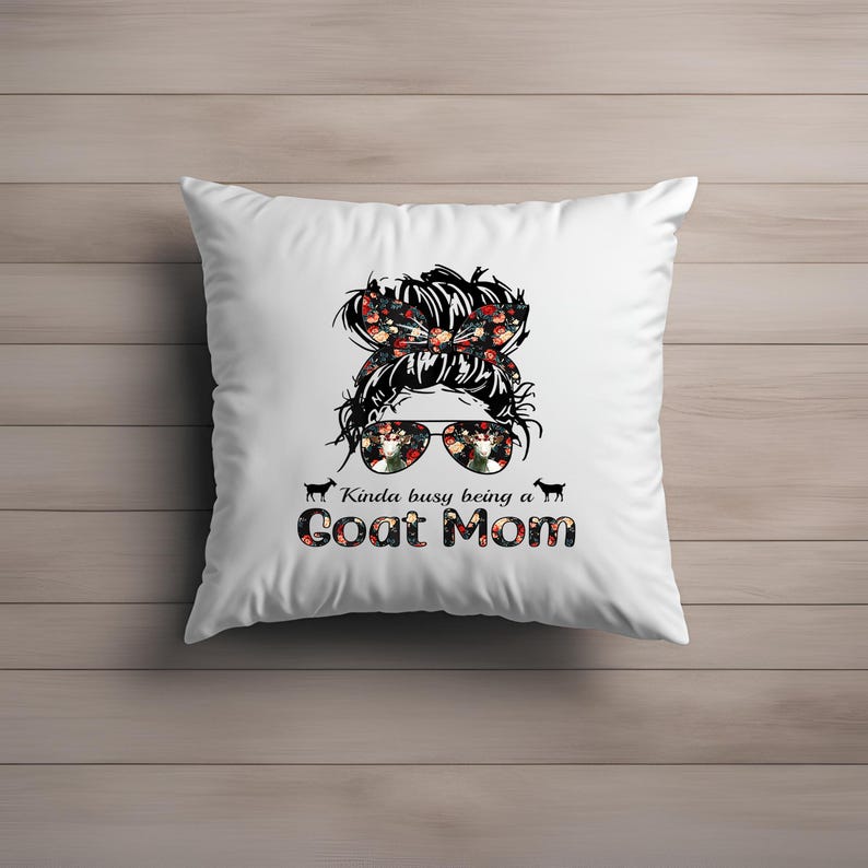 May include: White pillow with a black and white illustration of a woman with a messy bun and floral accents. The woman is wearing sunglasses and the text "Kinda busy being a Goat Mom" is below the illustration.
