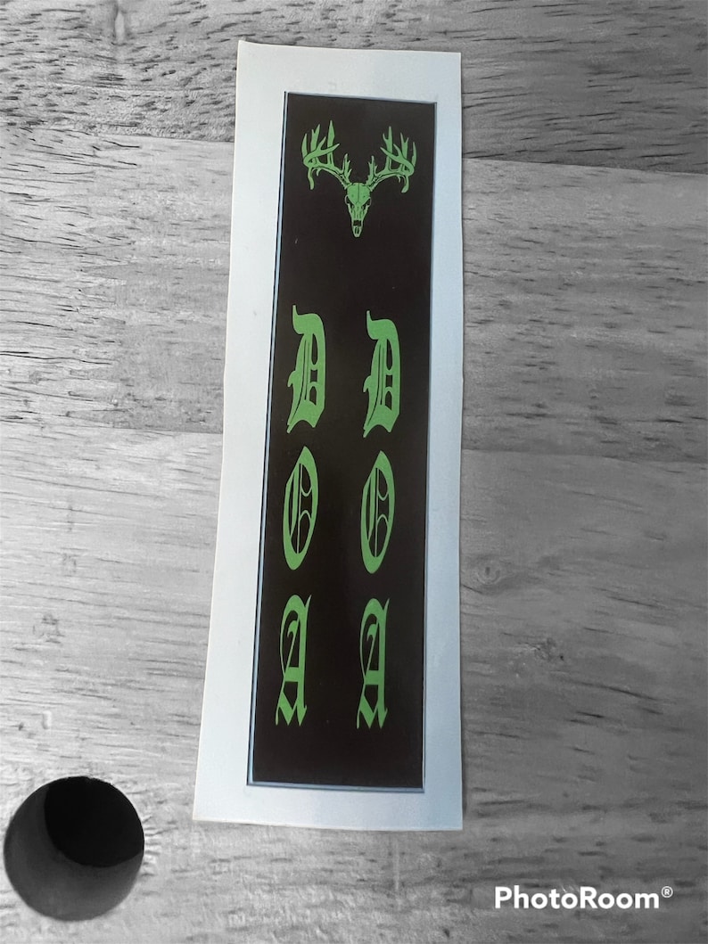 K&ouml;nnte beinhalten: Ein schwarzer und gr&uuml;ner Aufkleber mit einem Hirschsch&auml;del und dem Wort "DOA" in gotischer Schrift.