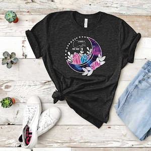 Op de afbeelding: Een donker grijs t-shirt met een halve maan-print. De maan is gevuld met een galaxy-print en heeft drie roze en blauwe kristallen erin. De tekst "Ik heb een kristal voor dat" staat op het shirt gedrukt.