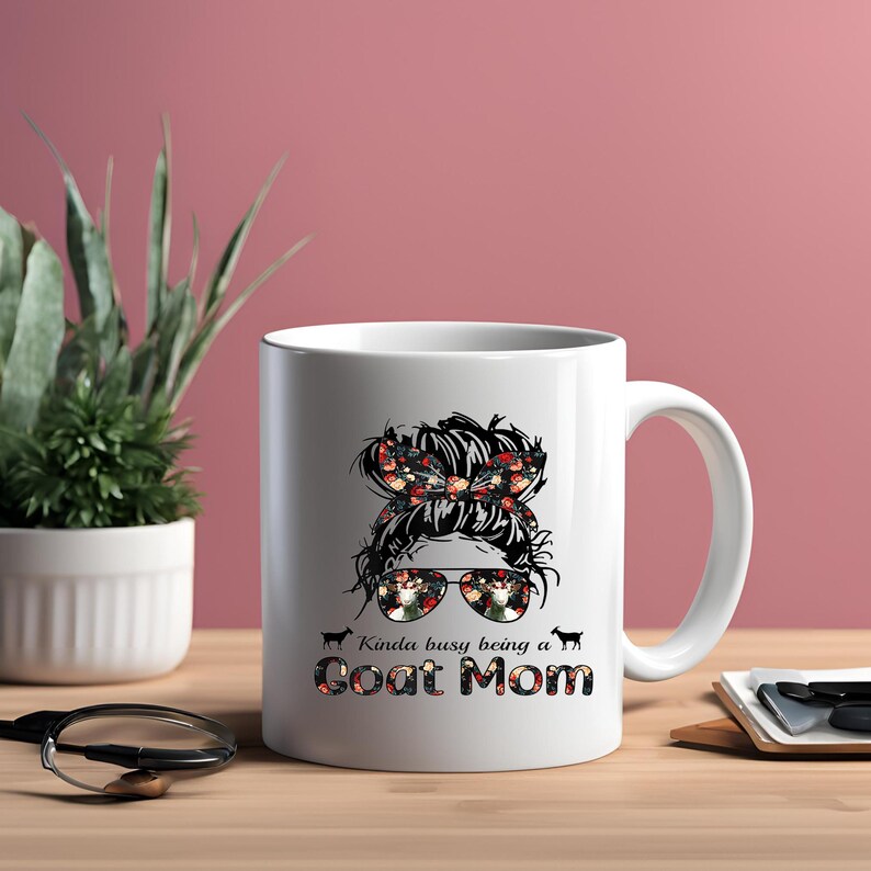 May include: White ceramic coffee mug with a black and white illustration of a woman with a messy bun and sunglasses. The woman's hair is decorated with a floral pattern. The text "Kinda busy being a Goat Mom" is printed below the illustration.