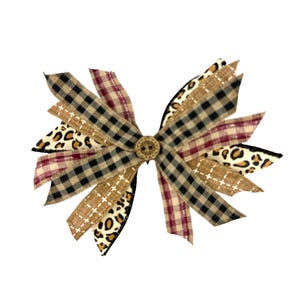 May include: A decorative hair bow featuring a variety of patterned ribbons. The bow includes black and tan plaid, leopard print, and burgundy plaid ribbons. A small, round, wooden button is at the center of the bow.