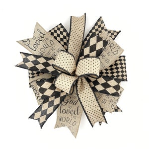 May include: A decorative bow with a mix of patterned ribbons. The bow features ribbons with black and tan harlequin, polka dot, and text that reads "For God so loved the world that He gave His".