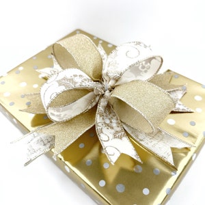 May include: A gold gift box with white polka dots topped with a large bow made of gold and white ribbon.