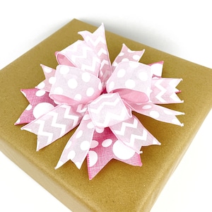 May include: A pink and white bow with polka dots and zig-zag patterns on a brown paper gift bag.
