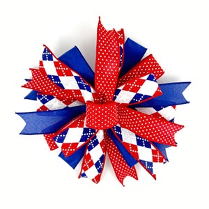 May include: A red, white, and blue bow with a checkered pattern and white polka dots. The bow is made of ribbon and is tied in a knot.