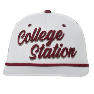 Könnte beinhalten: Weiße Baseballkappe mit dem in bordeauxfarbener Schrift gestickten Schriftzug "College Station". Die Kappe hat einen bordeauxfarbenen Schirm und einen bordeauxfarbenen Knopf. Ein stilvolles Accessoire für College Station-Fans.