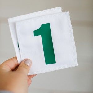 Op de afbeelding: Witte stoffen label met een groen nummer één erop gedrukt.