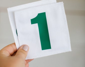 Pode incluir: Etiqueta de tecido branco com um número um verde impresso nela.
