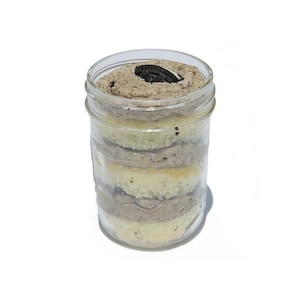 Peut inclure: Un bocal en verre rempli de couches de gâteau, de glaçage et d'un Oreo sur le dessus. Le gâteau est blanc et le glaçage est de couleur brun clair.