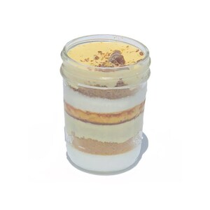 Può includere: Un barattolo di vetro pieno di strati di un dessert. Il dessert è fatto con una base di briciole di colore marrone chiaro, uno strato bianco, uno strato giallo e una copertura di colore marrone chiaro. Il barattolo ha un coperchio di vetro trasparente.
